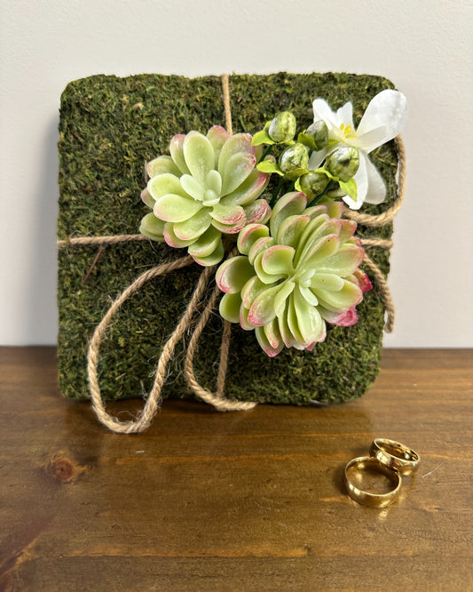 Almofadinha para alianças com base de grama sintética e flores plásticas. Modelo Graminha da Etiquette, perfeito para cerimônias no campo.