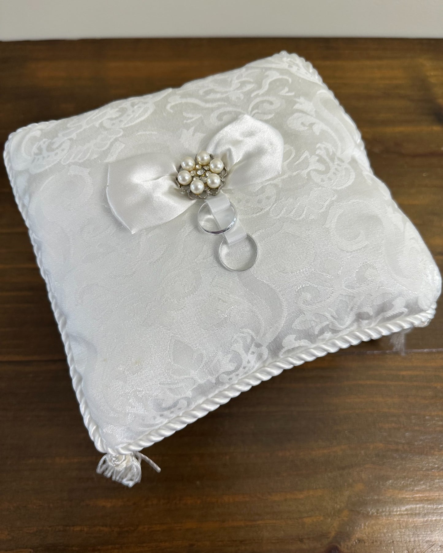 Almofadinha brocado da Etiquette com laço central de pérolas e cristais, fitas para alianças e franjas nas pontas. Modelo clássico e sofisticado.