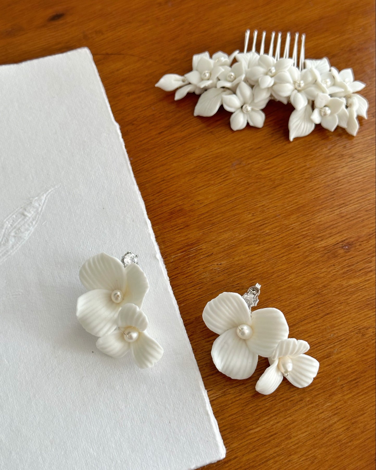 Brinco com duas flores de porcelana fria com detalhes em pérola no miolo da flor e pingo de luz de zircônia no pino, medindo 4,5 cm de comprimento.