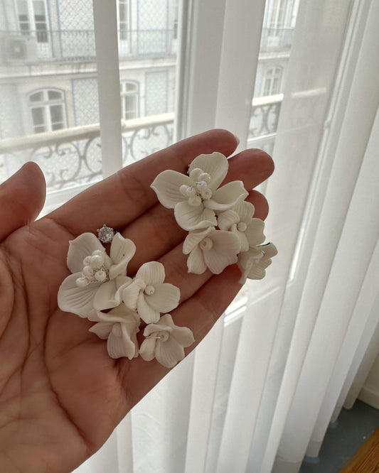 Brinco com mix de flores de porcelana fria com detalhes em miçangas brancas e pingo de luz de zircônia no pino, medindo 4,5 cm de comprimento.