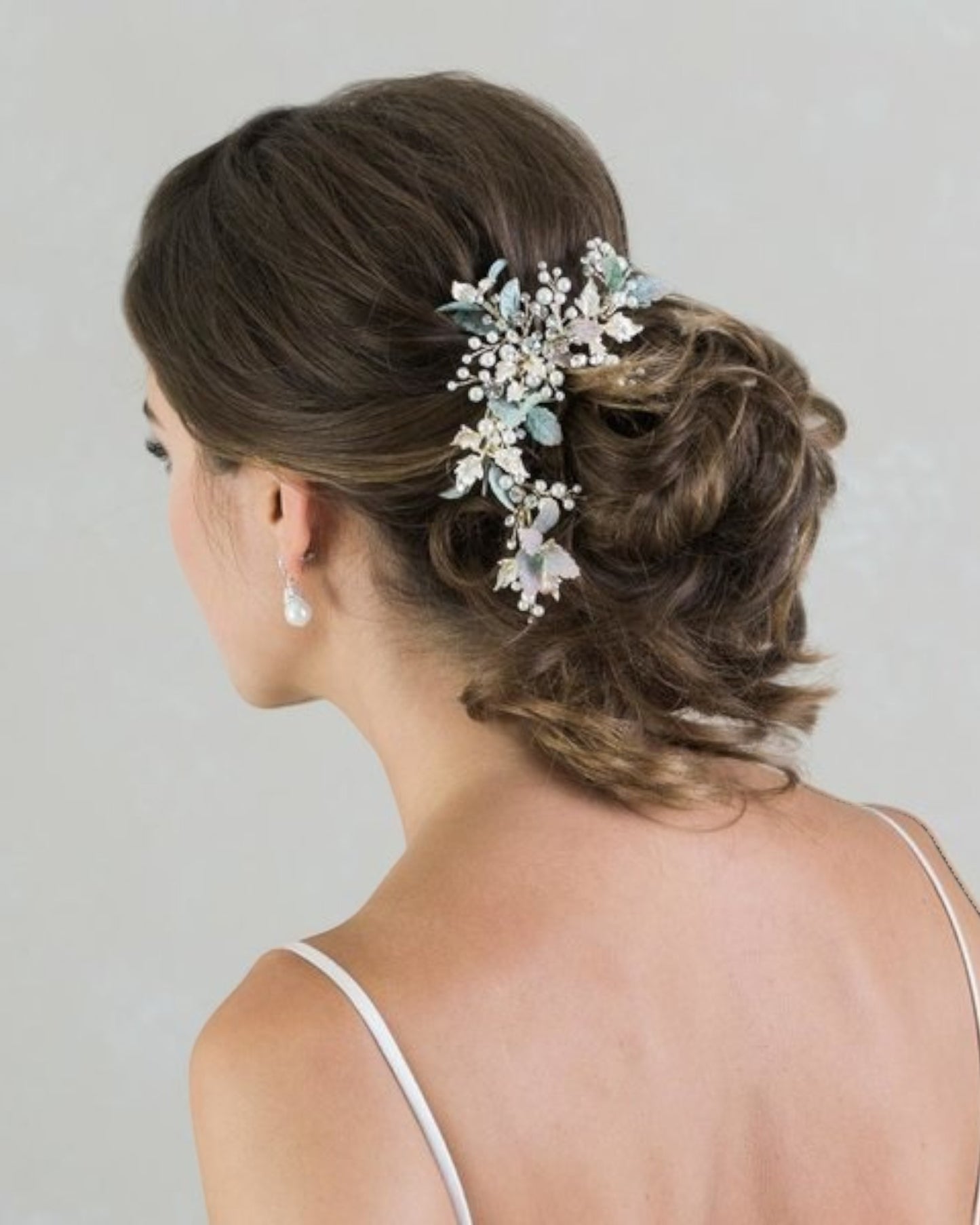 Um lindo e assimétrico pente para noivas com base em metal no tom champagne que combina delicadas folhas verdes com ramos de pérolas e strass. Uma sugestão perfeita para o casamento no campo.