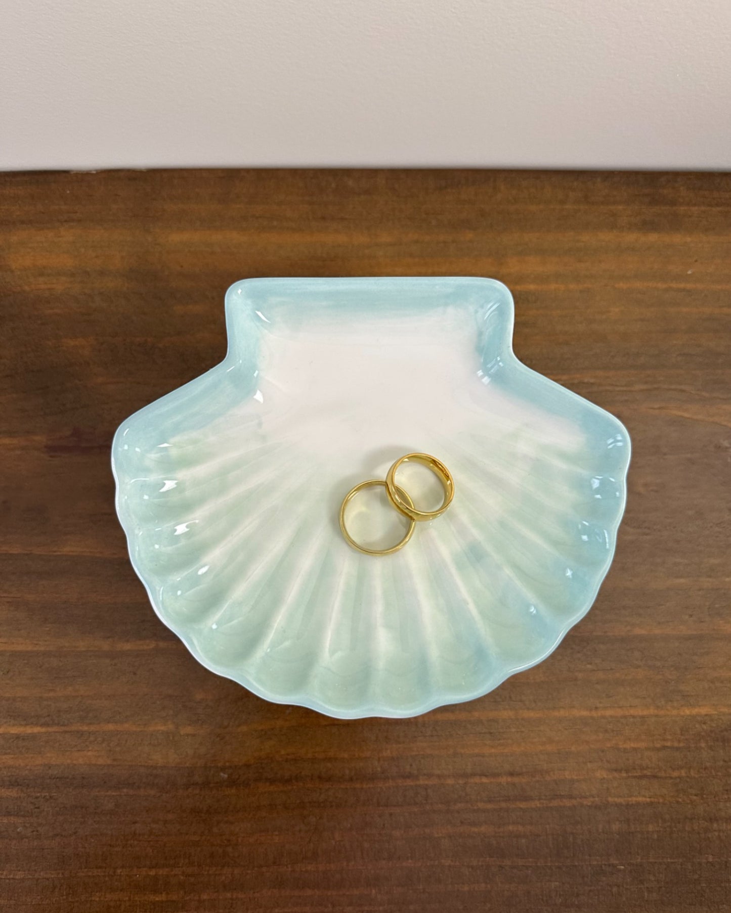 Pratinho porta-alianças da Etiquette em formato de concha, em cerâmica branca com pintura azul clara. Modelo leve e delicado para cerimônias à beira-mar.