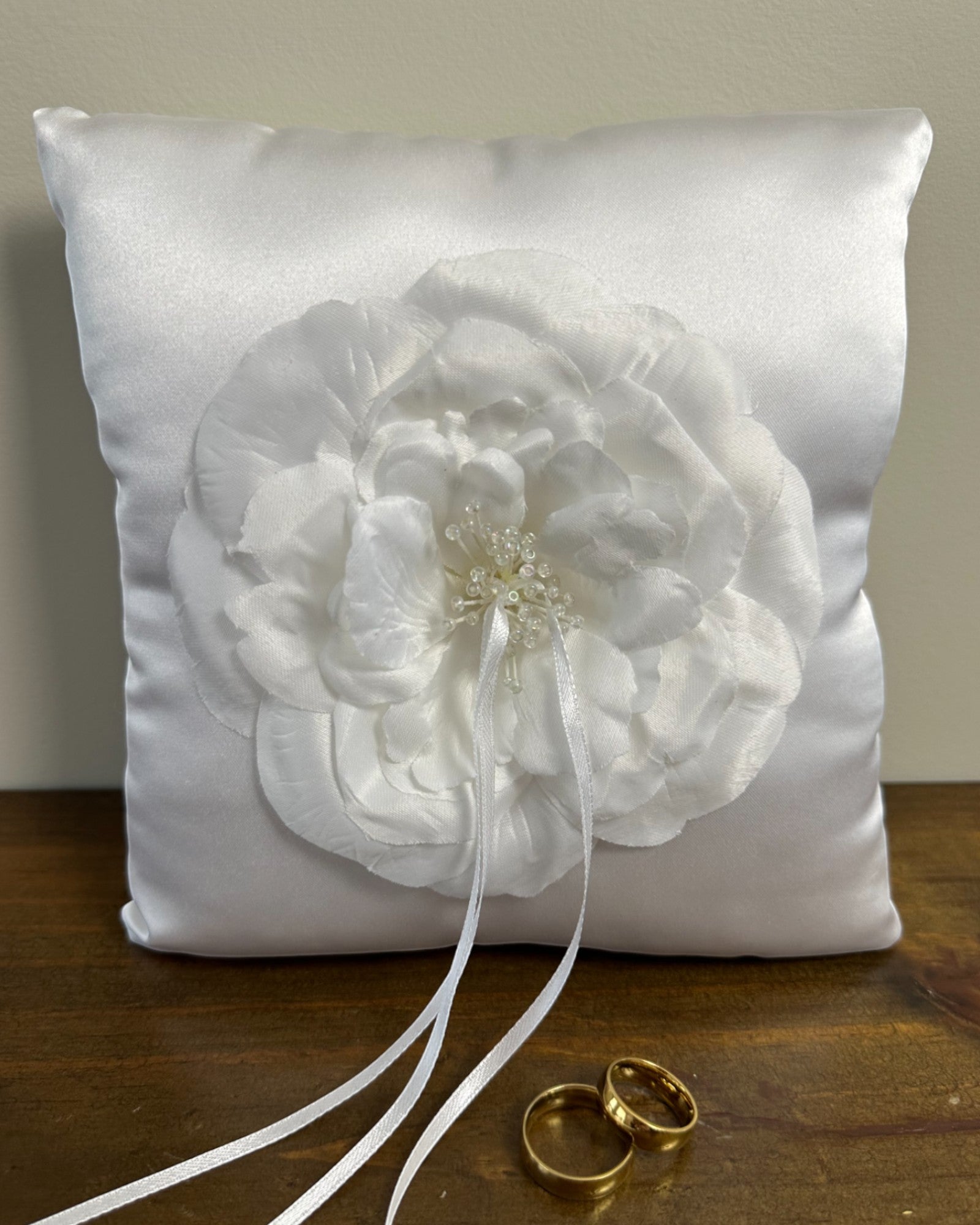 Almofadinha para alianças em cetim branco com flor aplicada no centro e miçangas no miolo. Modelo clássico e elegante da Etiquette.