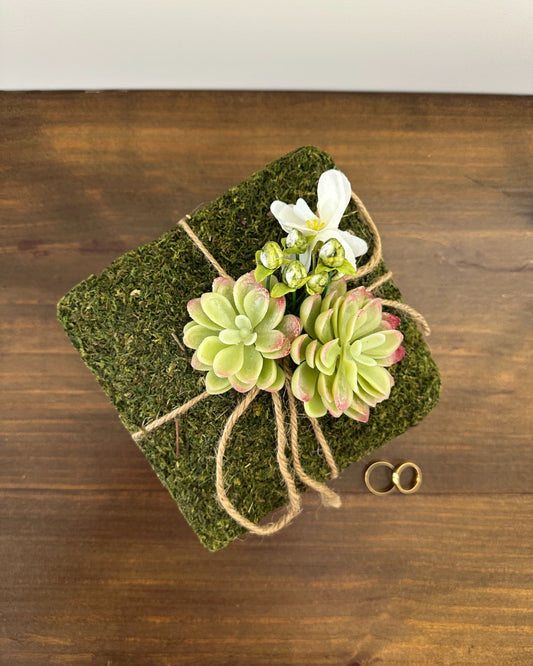 Almofadinha para alianças com base de grama sintética e flores plásticas. Modelo Graminha da Etiquette, perfeito para cerimônias no campo.