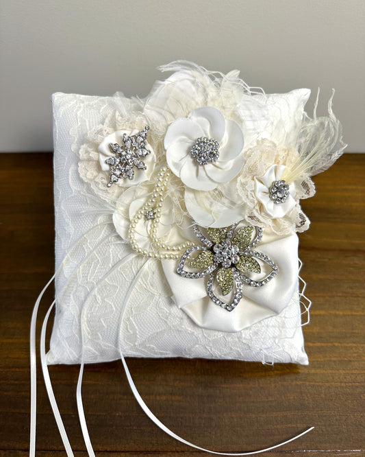 Almofadinha Genevieve da Etiquette, com cetim, renda offwhite, flores de tecido, plumas e cristais. Ideal para cerimônias sofisticadas.