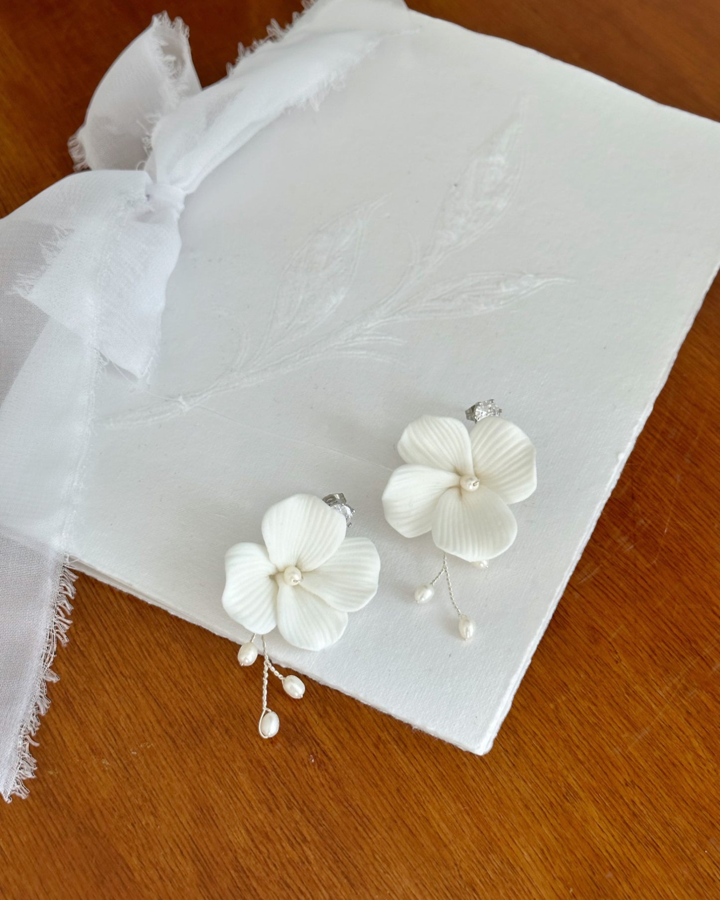 Brinco de flor de porcelana fria com raminho de metal prata com pérolas de água doce e pingo de luz de zircônia no pino, medindo 6 cm de comprimento.