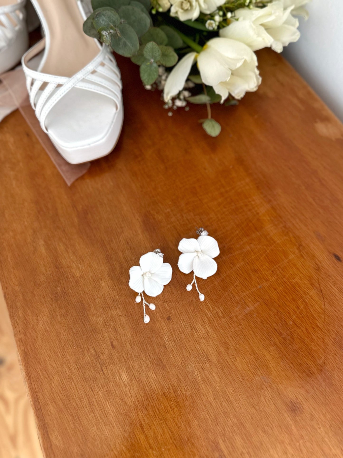Brinco de flor de porcelana fria com raminho de metal prata com pérolas de água doce e pingo de luz de zircônia no pino, medindo 6 cm de comprimento.