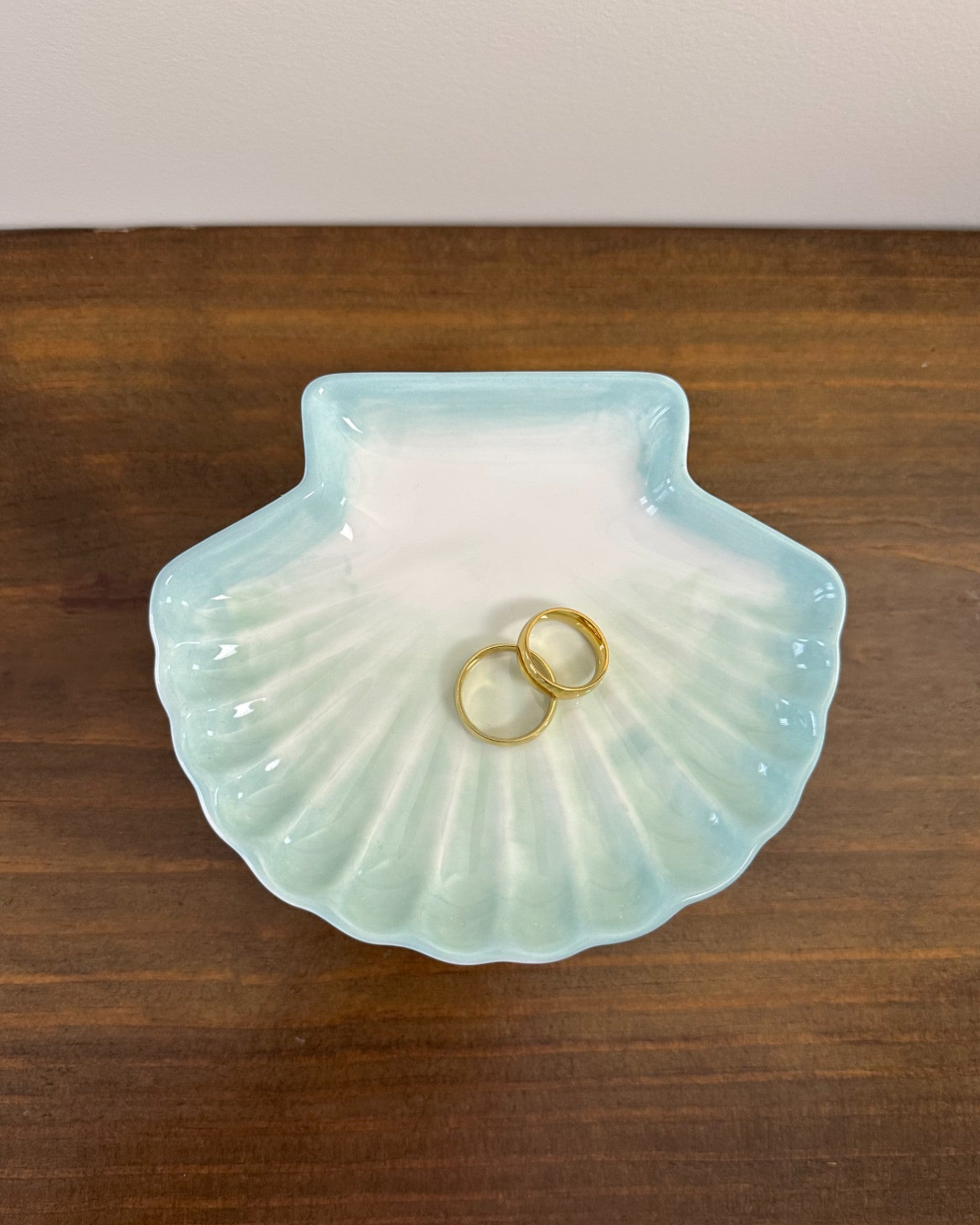 Pratinho porta-alianças da Etiquette em formato de concha, em cerâmica branca com pintura azul clara. Modelo leve e delicado para cerimônias à beira-mar.