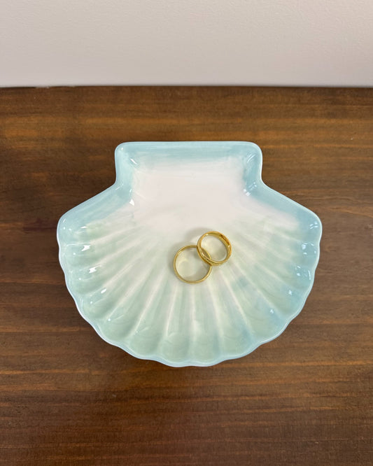 Pratinho porta-alianças da Etiquette em formato de concha, em cerâmica branca com pintura azul clara. Modelo leve e delicado para cerimônias à beira-mar.